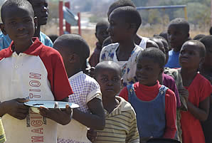 Time for lunch. Children with happy faces line up with their plates to get a plate of sadza and meat